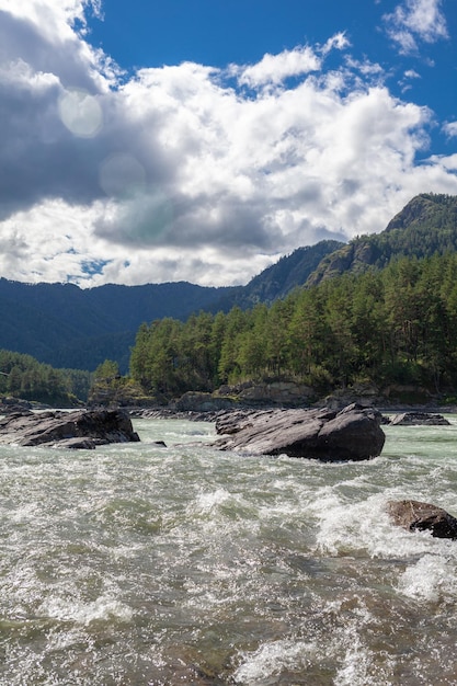 Um grande rio de montanha largo e cheio de fluxo rápido. Grandes rochas saem da água.