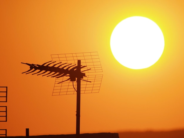 Um grande sol está se pondo atrás de uma antena de tv.