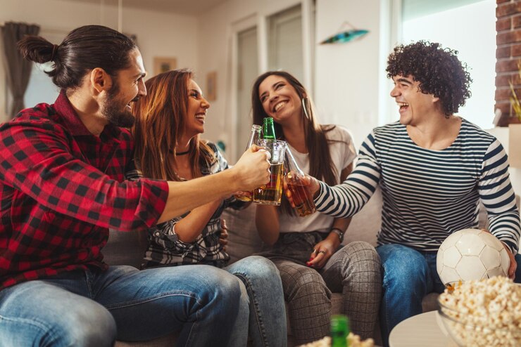 Foto um grupo de amigos assiste à transmissão de um evento esportivo. sentam-se em frente à tv da sala, comem lanche, bebem cerveja e torcem pelo time favorito.