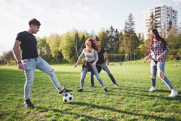 Um grupo de amigos com roupas casuais joga futebol ao ar livre. As pessoas se divertem e se divertem. Descanso ativo e pôr do sol cênico