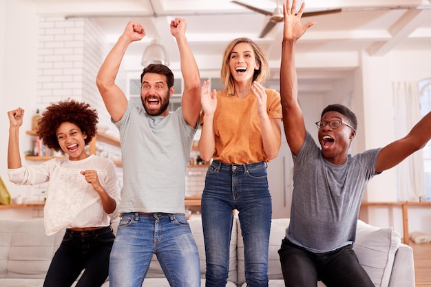 Um grupo de amigos entusiasmados sentados no sofá a ver desporto na televisão e a celebrar.