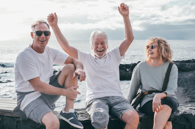 Um grupo de amigos maduros e idosos despreocupados sentados à beira-mar. Três pessoas ficam juntas a divertir-se.