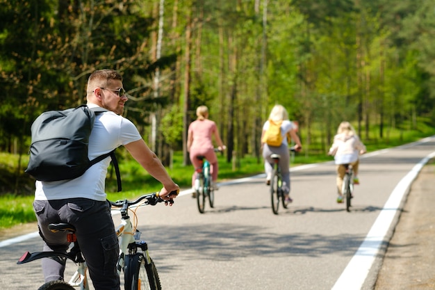 Um grupo de ciclistas com mochilas anda de bicicleta em uma estrada florestal curtindo a natureza.