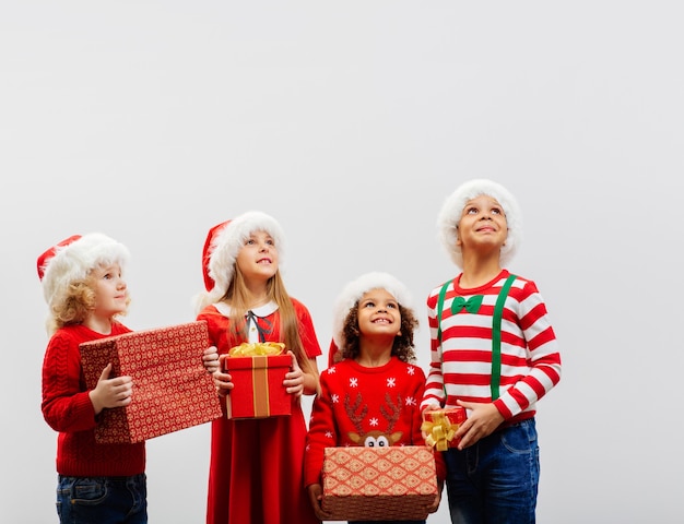 Um grupo de crianças com presentes de Natal nas mãos está fantasiado olha para cima com interesse