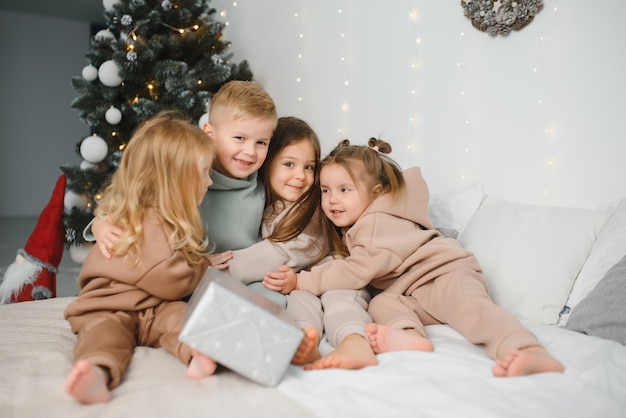 Um grupo de crianças debaixo de uma árvore de Natal em casa. Meninos e meninas em fantasias extravagantes celebram as férias de inverno. As crianças abrem os presentes junto à lareira.