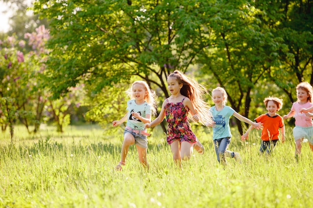 Um grupo de crianças felizes de meninos e meninas corre no parque na grama em um dia ensolarado de verão.