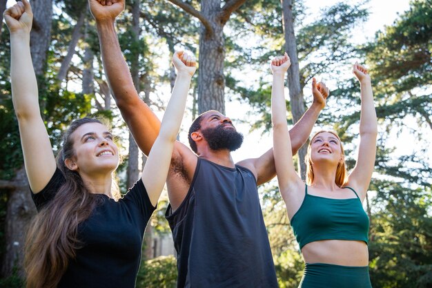 Um grupo de desportistas estão felizes com as mãos levantadas no ar durante um treino estilo de vida saudável