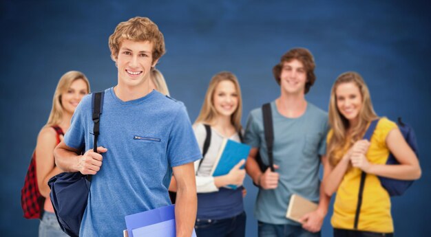 Um grupo de estudantes universitários sorridentes olha para a câmera enquanto um homem fica na frente contra o quadro-negro azul