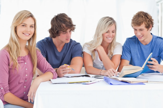 Um grupo de estudo trabalhando duro quando uma garota sorri e olha para a câmera