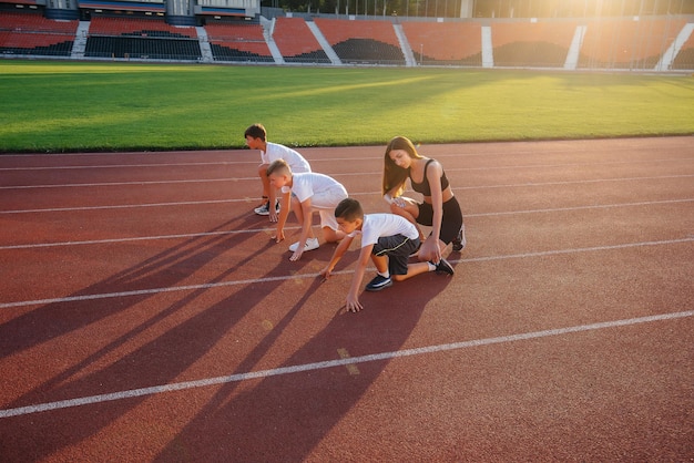 Um grupo de filhos de meninos é ensinado por um treinador no início antes de correr no estádio durante o pôr do sol Um estilo de vida saudável