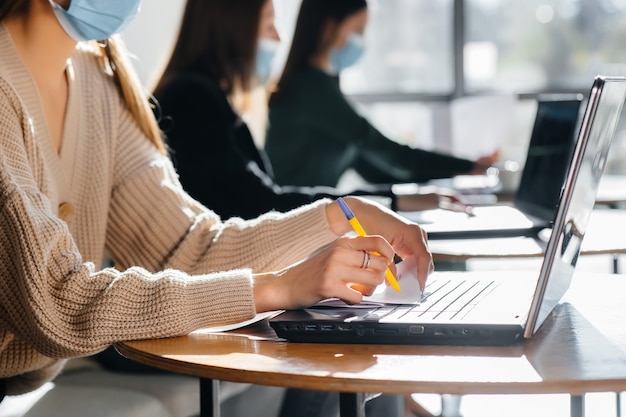 Um grupo de garotas mascaradas mantém uma distância social em um café enquanto trabalha com laptops