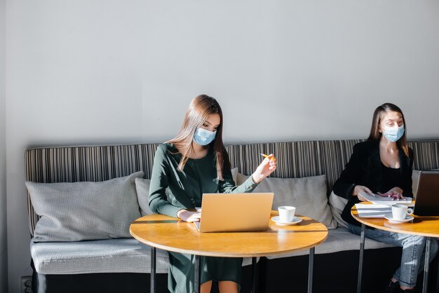 Um grupo de garotas mascaradas mantém uma distância social em um café enquanto trabalha com laptops.