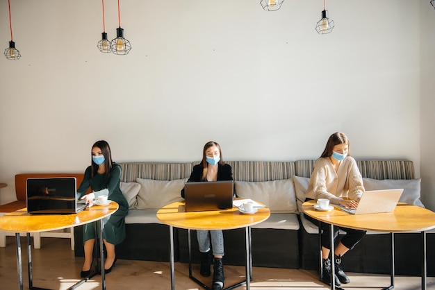 Um grupo de garotas mascaradas mantém uma distância social em um café enquanto trabalha com laptops.