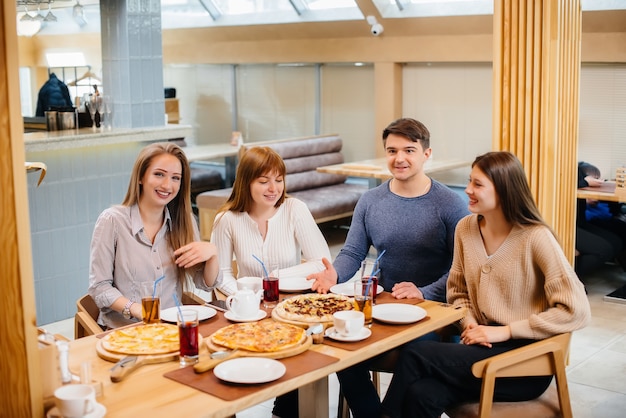 Um grupo de jovens amigos alegres está sentado em um café conversando e comendo pizza