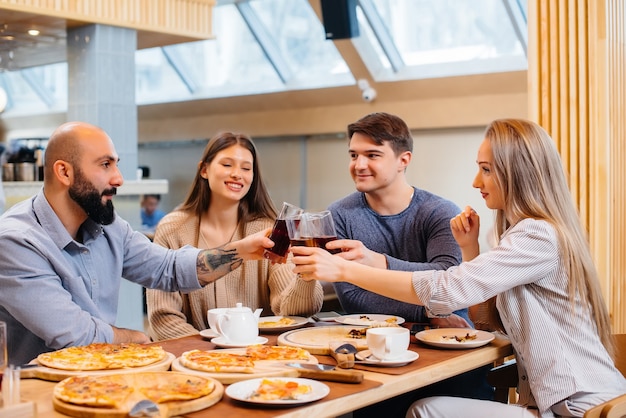 Um grupo de jovens amigos alegres está sentado em um café conversando e comendo pizza