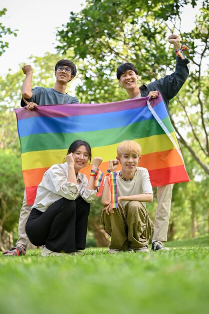 Um grupo de jovens amigos asiáticos felizes com a bandeira do arco-íris LGBT ao ar livre