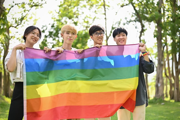 Um grupo de jovens amigos universitários asiáticos está segurando uma bandeira LGBTQ do arco-íris ao ar livre