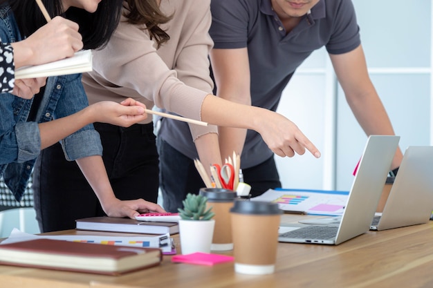 Um grupo de jovens empresários se encontra em um laptop e trabalha em um escritório interno.