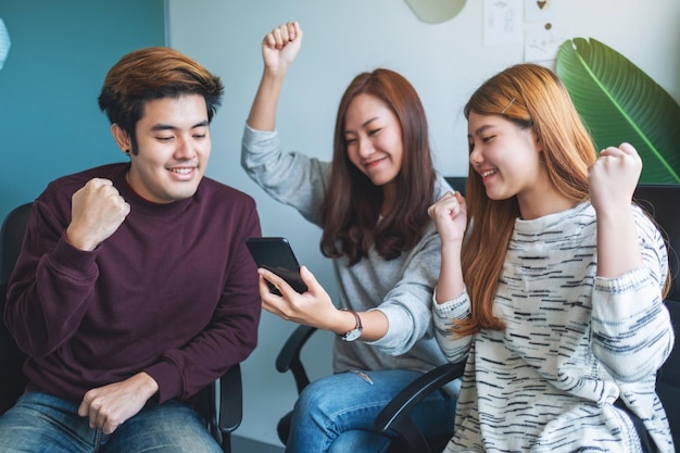 Um grupo de jovens se divertindo e comemorando enquanto assistem e jogam no celular juntos