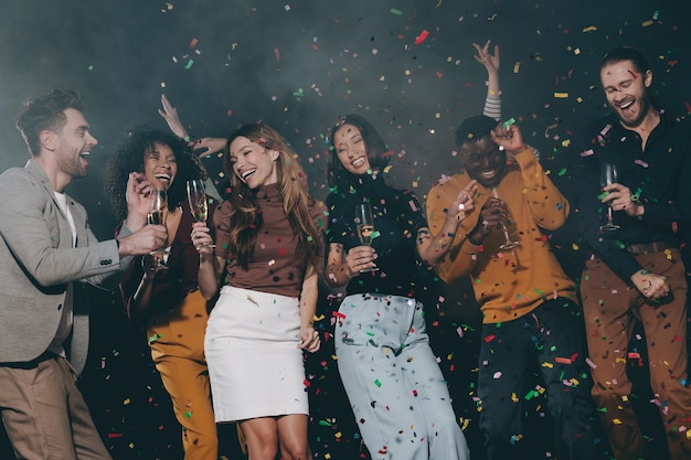 Um grupo de jovens sorridentes desfrutando de uma festa de Ano Novo no clube noturno com confetes voando ao redor