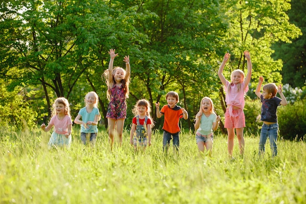 Um grupo de meninos e meninas crianças felizes correndo no parque na grama em um dia ensolarado de verão.