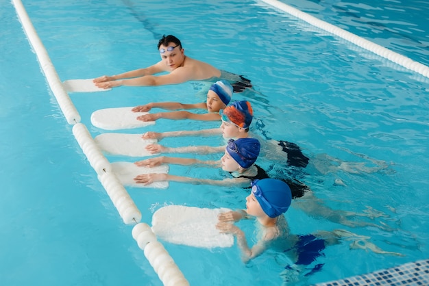 Um grupo de meninos e meninas treina e aprende a nadar na piscina com um instrutor. Desenvolvimento de esportes infantis.