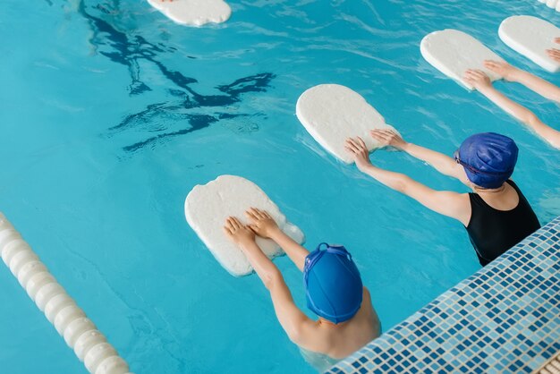 Um grupo de meninos e meninas treina e aprende a nadar na piscina com um instrutor. desenvolvimento de esportes infantis.