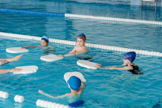 Um grupo de meninos e meninas treina e aprende a nadar na piscina com um instrutor. Desenvolvimento de esportes infantis.