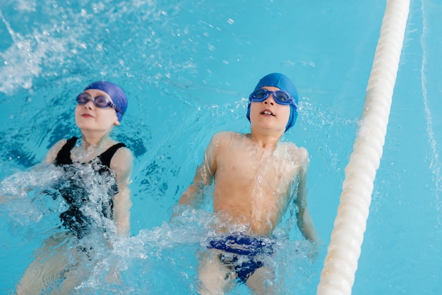 Um grupo de meninos e meninas treina e aprende a nadar na piscina com um instrutor. Desenvolvimento de esportes infantis.