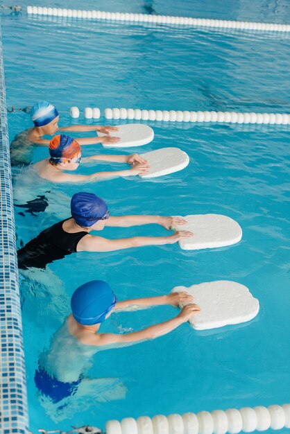 Um grupo de meninos e meninas treina e aprende a nadar na piscina com um instrutor. Desenvolvimento de esportes infantis.