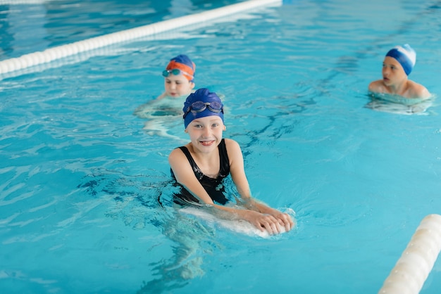 Um grupo de meninos e meninas treina e aprende a nadar na piscina com um instrutor. Desenvolvimento de esportes infantis.