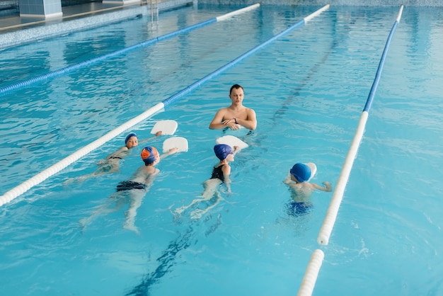 Um grupo de meninos e meninas treina e aprende a nadar na piscina com um instrutor. Desenvolvimento de esportes infantis.