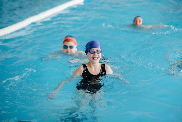 Um grupo de meninos e meninas treina e aprende a nadar na piscina com um instrutor. Desenvolvimento de esportes infantis.