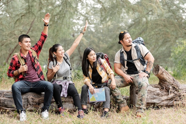 Um grupo de mochileiros asiáticos, homens e mulheres, olhou e ergueu as mãos, convidando aqueles que haviam se reunido para sentar nas toras da floresta.