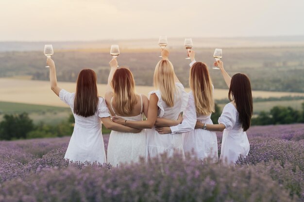 Um grupo de mulheres em vestidos brancos segura taças de vinho em um campo