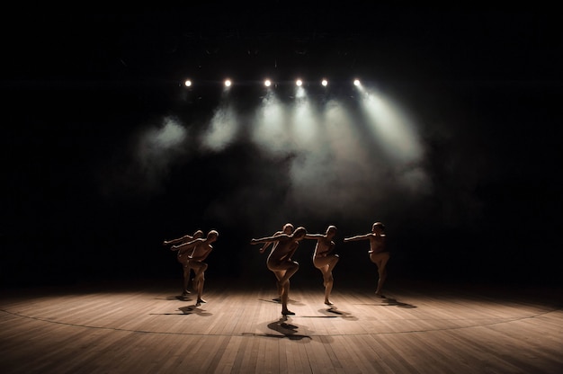 Foto um grupo de pequenos bailarinos ensaia no palco com luz e fumaça