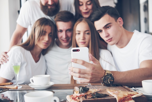 Um grupo de pessoas faz uma foto de selfie em um café. os melhores amigos reunidos em uma mesa de jantar comendo pizza e cantando várias bebidas