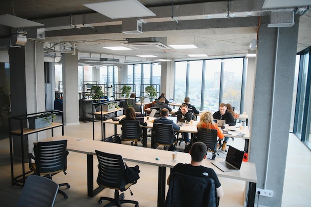 Um grupo de pessoas sentadas em mesas em um grande espaço de escritório aberto