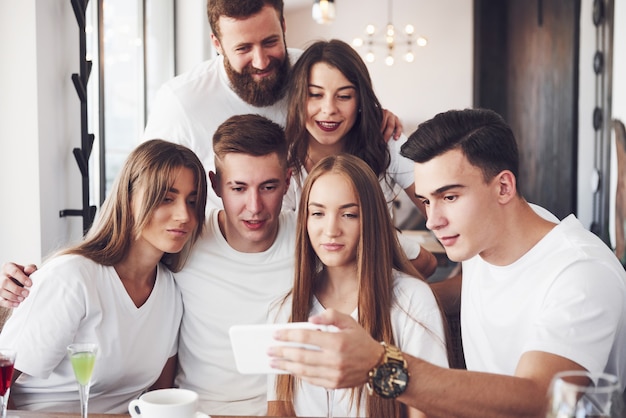 Um grupo de pessoas tira uma foto de selfie em um café. Os melhores amigos se reuniram em uma mesa de jantar comendo pizza e cantando vários drinks.