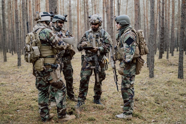 Um grupo de soldados barbudos de meia-idade em uniformes e coletes táticos discute o plano de ação