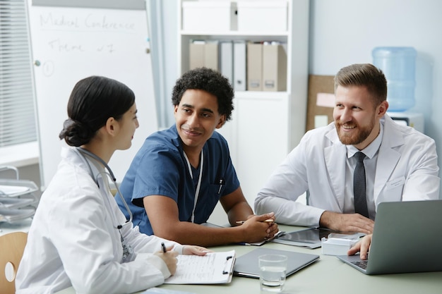 Um grupo de três médicos sorridentes reunidos à mesa na clínica.