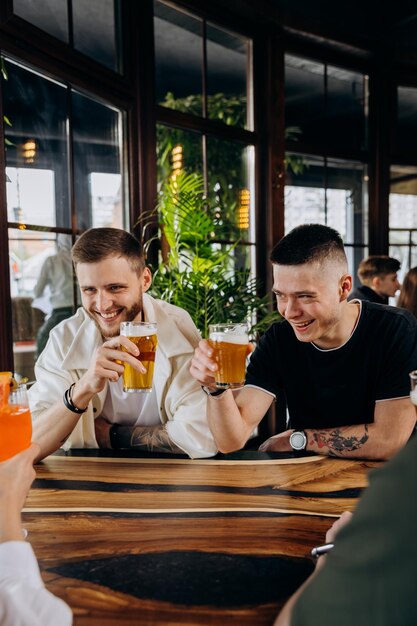 Um grupo feliz de amigos bebendo e tocando com cerveja e coquetéis no bar-restaurante da cervejaria conceito de estilo de vida de bebidas com meninos e meninas se divertindo juntos