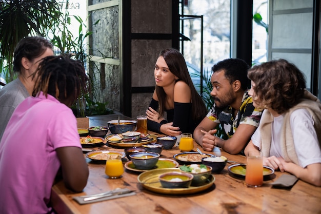 Um grupo multicultural de jovens em um café, comendo comida asiática, bebendo coquetéis, conversando