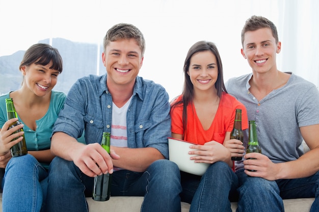 Um grupo sorridente sentado no sofá enquanto segura cervejas