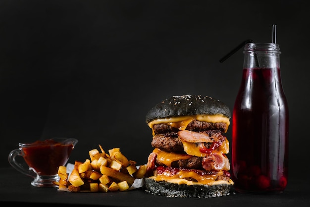 Um hambúrguer com batatas fritas, molho de tomate e copo de suco no fundo preto