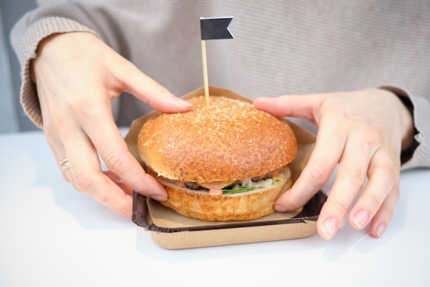 Um hambúrguer está deitado sobre uma mesa em um restaurante na frente de uma garota e come com as mãos.