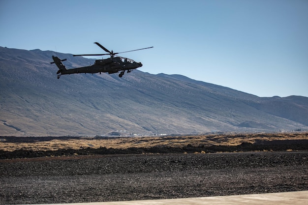 Um helicóptero sobrevoa um campo com montanhas ao fundo.