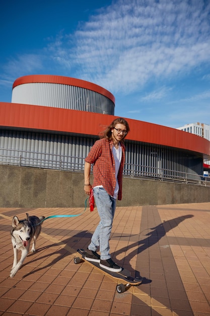 Um hipster a andar de skate com um cão na coleira a desfrutar do verão.