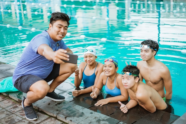 Um homem à beira da piscina tira uma selfie com quatro adolescentes vestindo maiôs em uma piscina