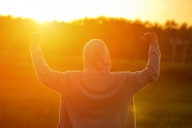 Foto um homem à luz do pôr do sol com as mãos para cima